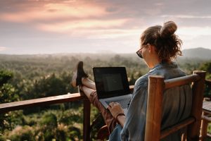 Young business woman working at the computer in cafe on the rock. Young girl downshifter working at a laptop at sunset or sunrise on the top of the mountain to the sea, working day.